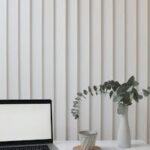 A clean and modern workspace featuring a laptop, vase with greenery, and notepad.